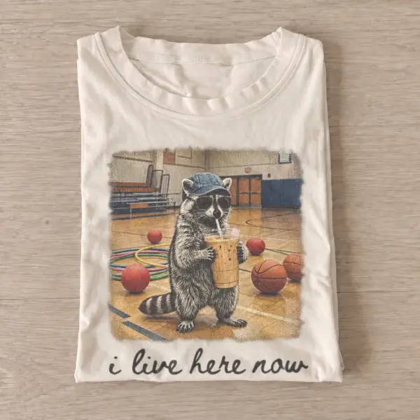 I live here now iced coffee raccoon t shirt sand20iced coffee raccoon.webp
